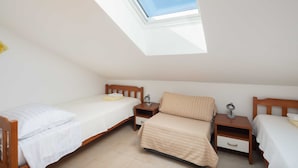 Une chambre de type dortoir avec deux lits simples, des tables de chevet en bois et un puits de lumière.