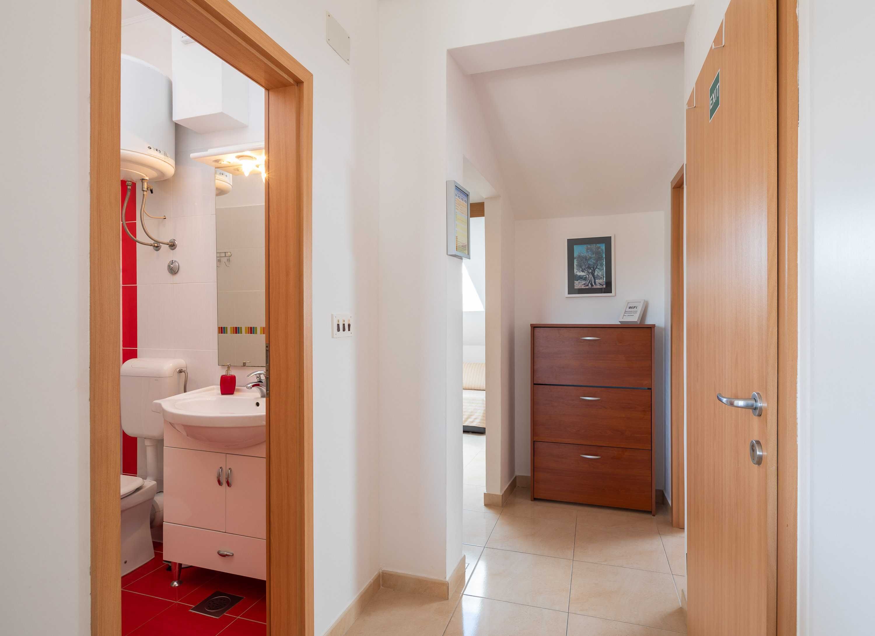 A hotel bathroom with a sink, toilet, and shower. There is a wooden door with a sign indicating the exit.