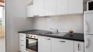 Une cuisine moderne avec des meubles blancs, un plan de travail noir, des appareils en acier inoxydable et une porte en verre donnant sur un espace extérieur.