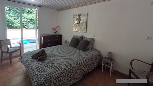 Un dormitorio con cama, mesita de noche, cómoda, silla y un cuadro en la pared.