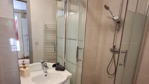 Un baño moderno con ducha de vidrio, lavabo blanco y espejo encima.