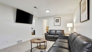 Ein Wohnzimmer mit einem Ecksofa, einem runden Couchtisch, einem flachbildfernseher an der Wand und einem gerahmten Bild.
