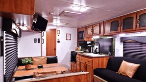 A compact RV interior with a kitchenette, a dining area, and a seating space.