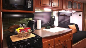 A compact kitchen with a microwave, stove, and wooden cabinets.