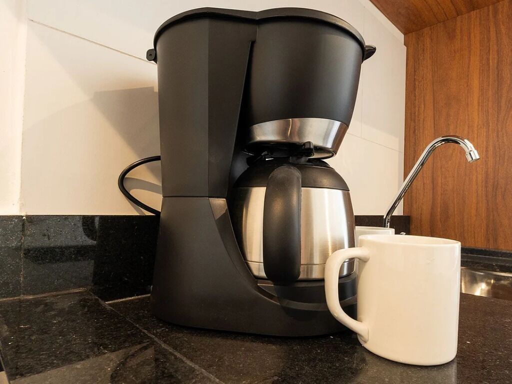 Une machine à café avec une tasse blanche posée sur un plan de travail noir.