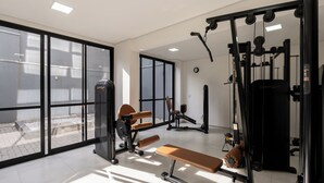 A gym with exercise equipment, large windows, and a bench. - Movi Life Torre 2 (São Paulo)