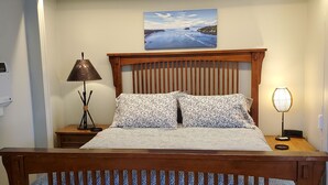 Een netjes opgemaakt bed met een houten hoofdbord, een nachtkastje met een lamp en een schilderij erboven.