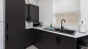 Une cuisine moderne avec des meubles de couleur sombre, un évier noir, un four à micro-ondes et une fenêtre équipée de stores.