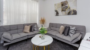 Un salon moderne avec deux canapés gris, une table basse ronde blanche et un vase décoratif contenant des plantes.