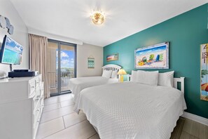 Hotellihuone, jossa on kaksi sänkyä, televisio, työpöytä ja näkymä rannalle.