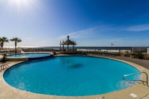 A large, clear blue pool with a gazebo and lounge chairs, surrounded by a deck and palm trees, overlooking the ocean. - Summer House 406B with Balcony (Orange Beach)