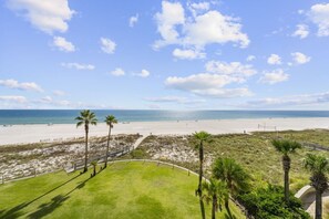 A beach view with a pathway leading to a grassy area with palm trees. - Summer House 406B with Balcony (Orange Beach)