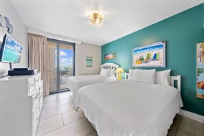 Habitación de hotel con dos camas, televisión, escritorio y vista al mar.