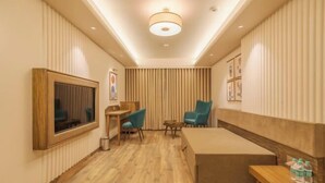 A hotel room with a bed, a desk, two chairs, a small table, a TV, and a ceiling light. - Phoenix Resort (Rajkot)