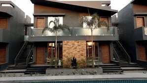 A modern multi-story building with a pool, outdoor seating, and a brick facade. - Phoenix Resort (Rajkot)