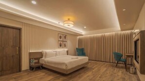 A modern hotel room with a large bed, a nightstand, a chair, and a wardrobe. - Phoenix Resort (Rajkot)