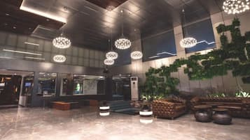 A spacious lobby with modern chandeliers, a seating area, and a large plant.