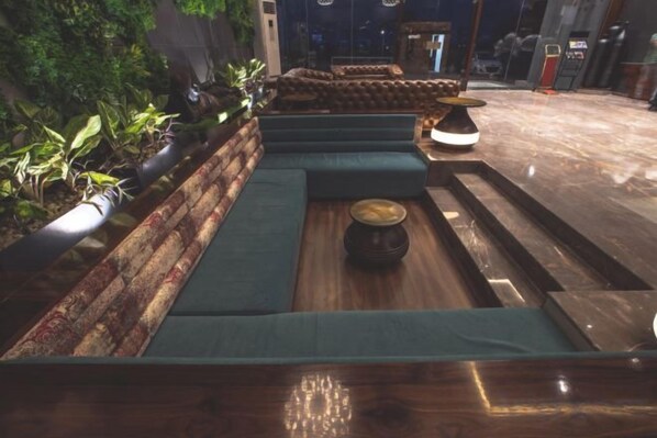 Una zona de estar con bancos acolchados y una mesa central, rodeada de plantas.