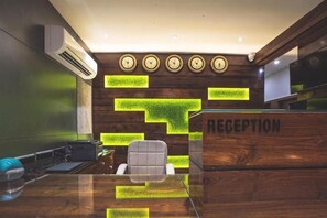 A reception desk with a wooden finish and a 'RECEPTION' sign, a modern chair, and a glass table. - Phoenix Resort (Rajkot)