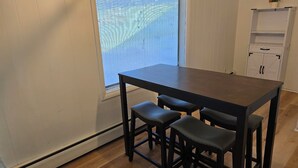 A small kitchen with a dark wooden table and three stools, a window with blinds, and a white cabinet with black handles. - Welcome to your getaway destination in Craig's rugged outdoors loving terrain. (Craig)