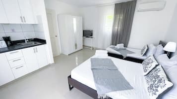 Een moderne hotelkamer met een keukenhoek, een bed met veel kussens, een televisie en een raam met gordijnen.