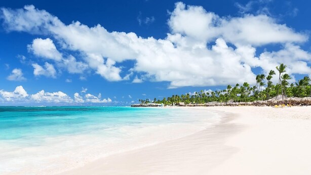 A beach with clear turquoise water, white sand, and palm trees under a blue sky with clouds. - GO TO THE BEACH STAYS (Punta Cana)