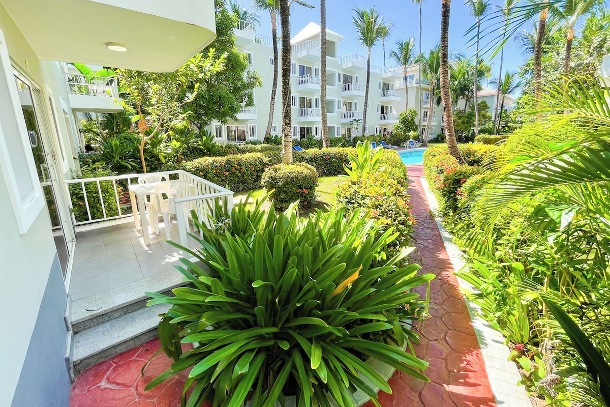 A hotel courtyard with a swimming pool, palm trees, and a well-maintained garden.