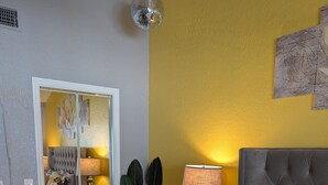 Ein Schlafzimmer mit einem Bett, Nachttischen, einem Spiegel, einer Pflanze und einer gelben Wand.