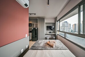 A modern hotel room with a bed, a small kitchenette, a TV, and a large window with a city view. - On Brooklin (São Paulo)