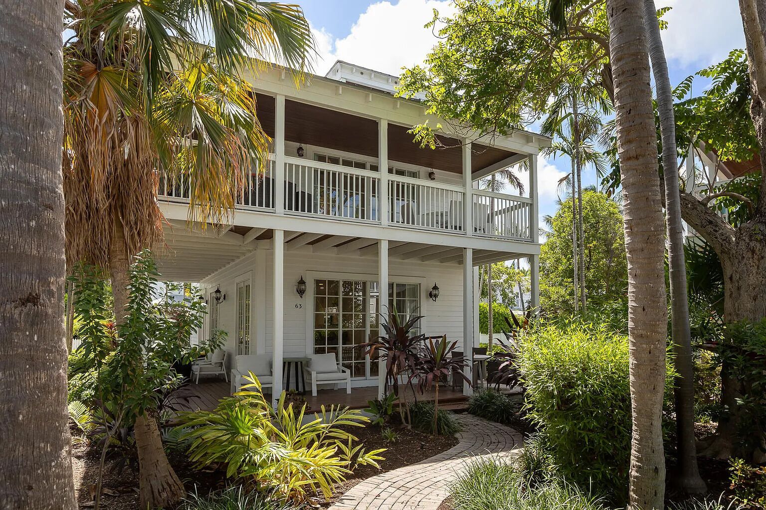 Une maison à deux étages dotée d’un balcon, entourée d’une végétation tropicale.