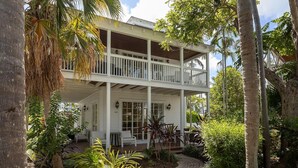 Een tweelaags huis met een balkon, omringd door tropische begroeiing.
