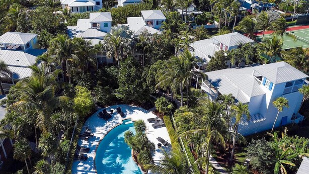Luchtbeeld van een resort met meerdere gebouwen, een centraal gelegen zwembad en omliggende palmbomen.