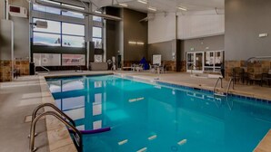 Un'ampia piscina coperta con corsie ben delimitate, una postazione di salvataggio e una zona relax con tavoli e sedie.