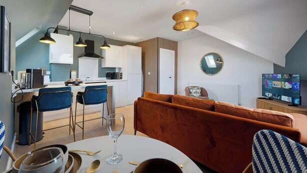 A modern kitchen with a dining area, a sofa, and a television.