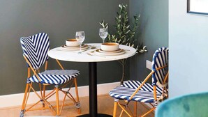 A dining area with a round table, two chairs, and a vase of greenery.