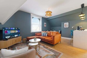 A modern living room with a television, sofa, coffee table, and a kitchen area with a bar.