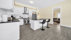 Una cocina moderna con armarios blancos, una isla central con taburetes de bar, horno empotrado y campana extractora de acero inoxidable.