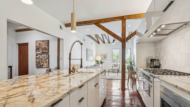 A modern kitchen with marble countertops, stainless steel appliances, and exposed wooden beams. - Ensign Loft 8 at Farragut Lofts (Bay Saint Louis)