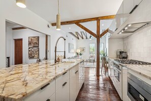 A modern kitchen with marble countertops, stainless steel appliances, and exposed wooden beams. - Ensign Loft 8 at Farragut Lofts (Bay Saint Louis)