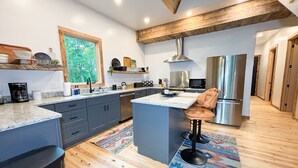 Una cucina moderna con mobili grigi, un'isola centrale, un frigorifero in acciaio inossidabile e un soffitto in legno.