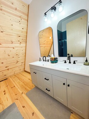 Une salle de bain moderne avec des murs recouverts de panneaux en bois, un meuble-lavabo blanc doté de deux vasques et un grand miroir.
