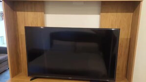 A flat-screen TV on a wooden TV stand with multiple shelves. - Top Floor URBN Loft (San José)