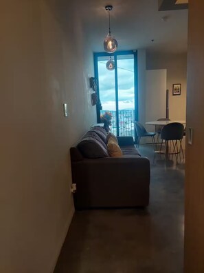 A modern living room with a sofa, a dining area with chairs, and a large window with a view. - Top Floor URBN Loft (San José)