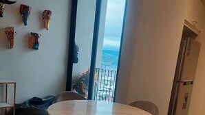 A modern dining area with a round table and four chairs, a large window with a view of the ocean, and a refrigerator to the right. - Top Floor URBN Loft (San José)