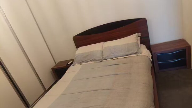 A neatly made bed with a wooden headboard, a grey bedspread, and two pillows. There is a nightstand with a lamp and a drawer. - Top Floor URBN Loft (San José)