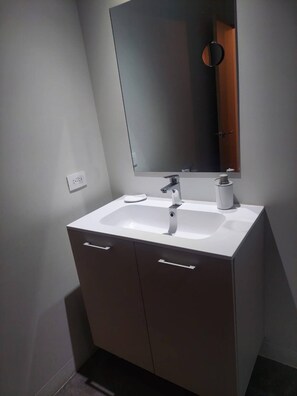 A modern bathroom with a white sink, a mirror, and a dark cabinet. - Top Floor URBN Loft (San José)