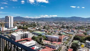 A cityscape with a prominent high-rise building, a mix of residential and commercial buildings, and a clear blue sky. - Top Floor URBN Loft (San José)