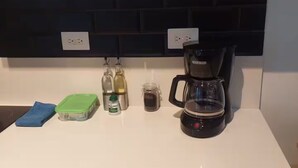 A kitchen with a white countertop, a coffee maker, a green storage container, a blue cloth, and a glass jar. - Top Floor URBN Loft (San José)