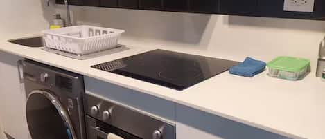 Une cuisine compacte dotée d’un lave-linge et d’un sèche-linge intégrés, d’un dosseret de carrelage noir et d’un plan de travail blanc.