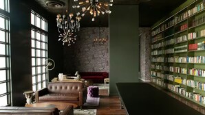 A library with leather sofas, a red sofa, a large bookshelf, and a chandelier. - Catorce Urbano (San José)